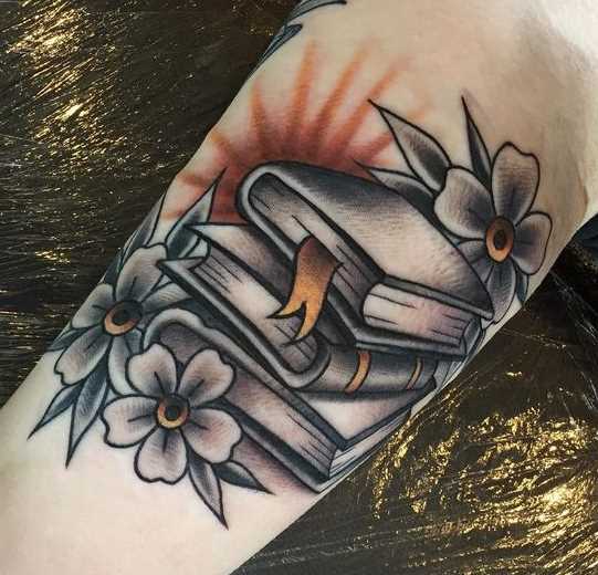 Tatuagem de livros com flores no antebraço da menina