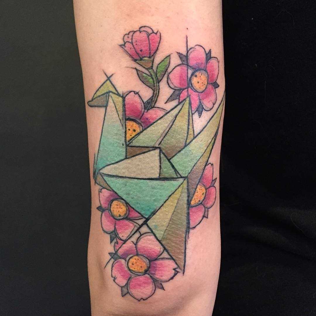 Tatuagem de origami-guindaste com flores na mão de uma mulher