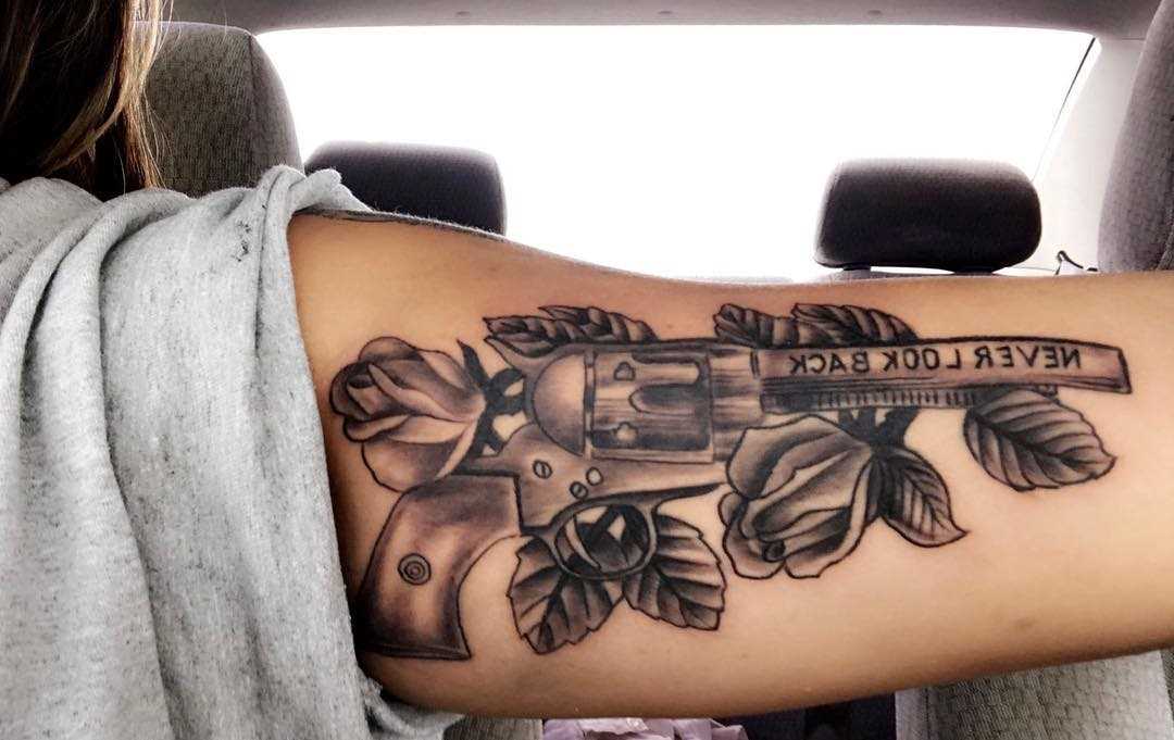 Tatuagem de revólver com rosas na mão da menina