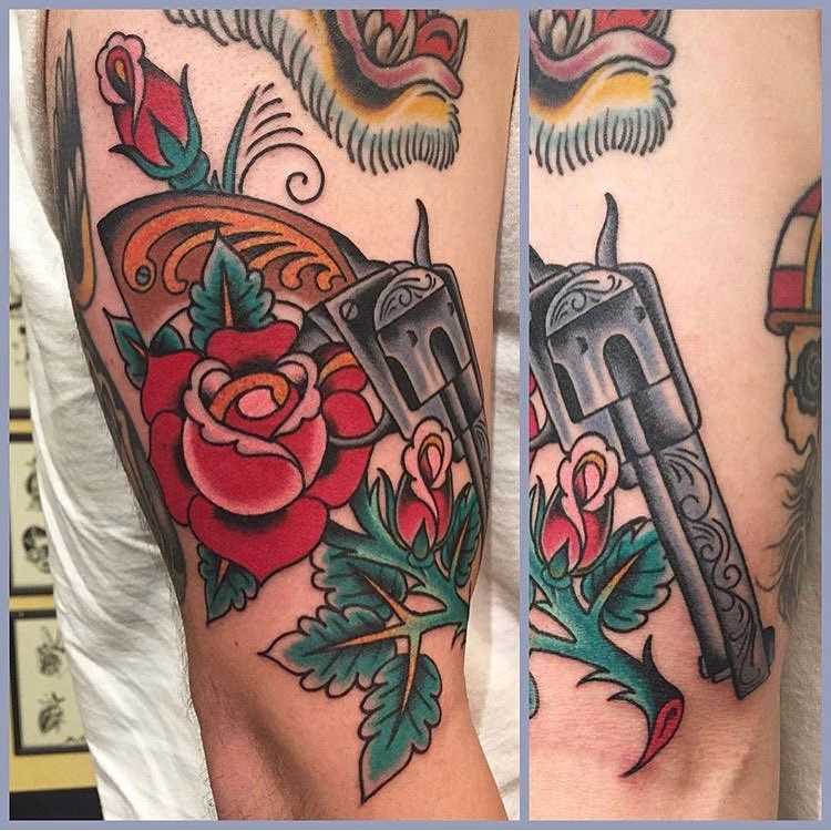 Tatuagem de revólver com rosas na mão de um cara