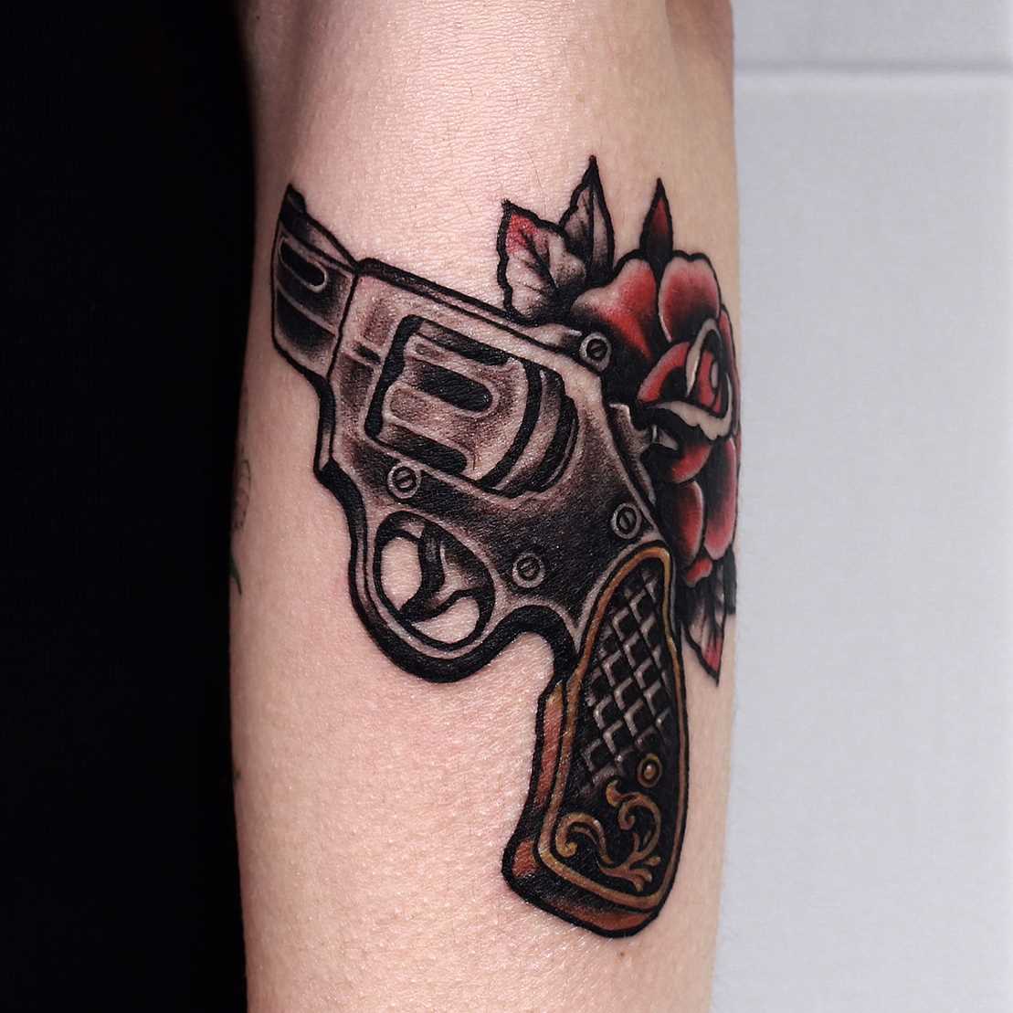 Tatuagem de revólver com uma rosa no antebraço cara