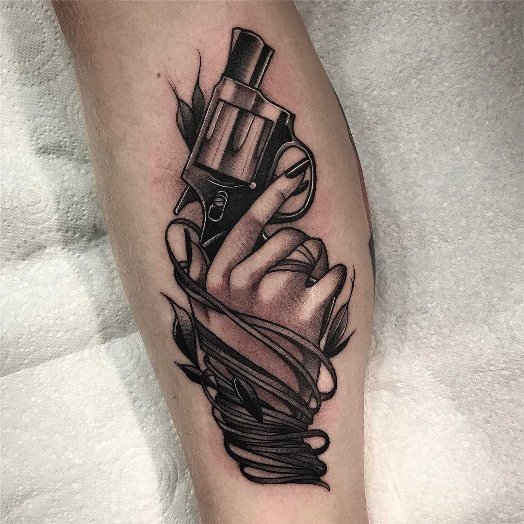 Tatuagem de revólver na mão sobre a perna de um cara