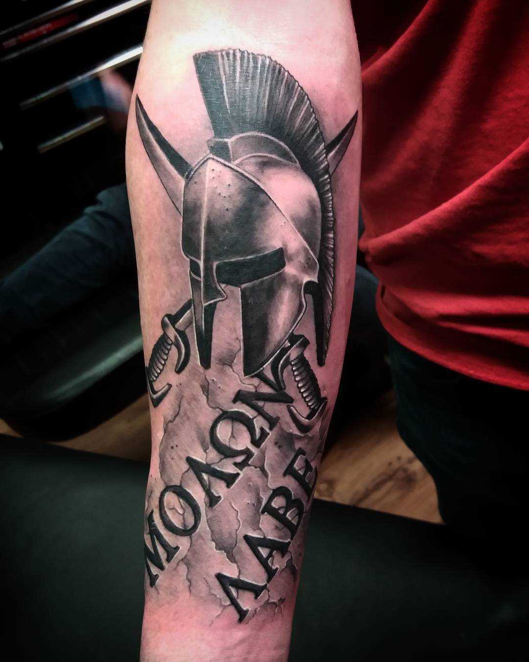 Tatuagem de um capacete espartano com a inscrição no antebraço homens