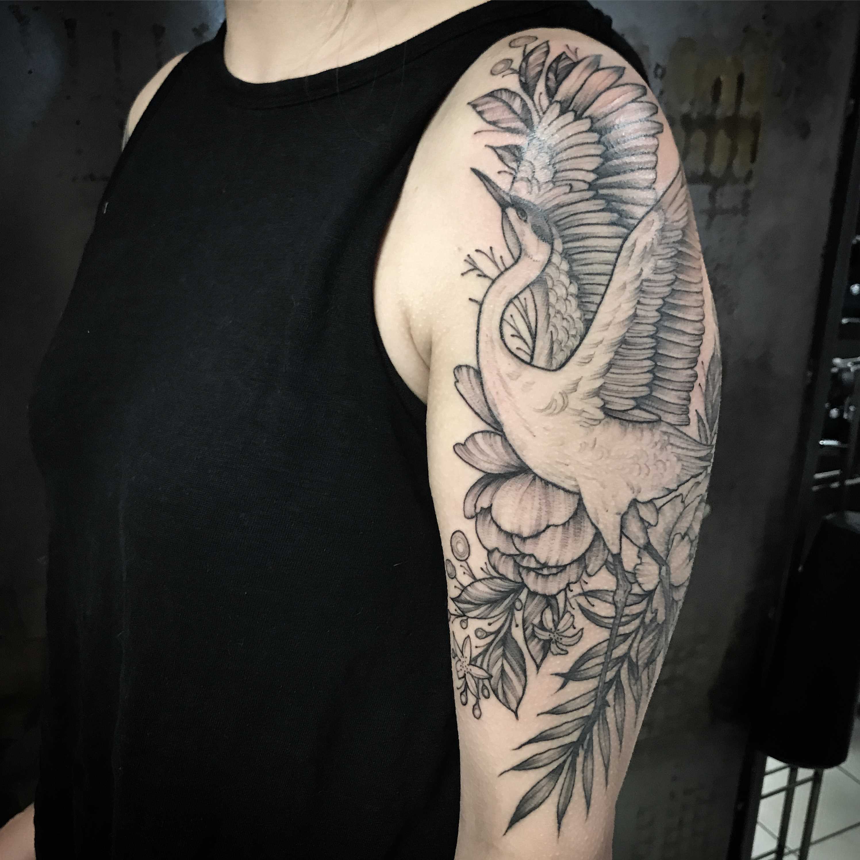 Tatuagem de um guindaste com flores no ombro da menina