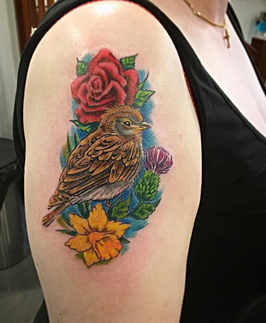 Tatuagem de um pardal com flores no ombro da menina