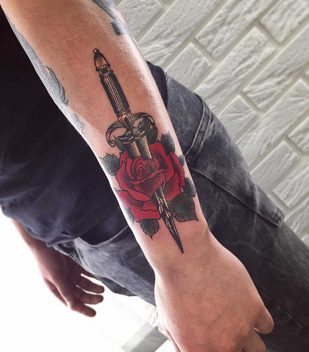 Tatuagem adaga com uma rosa no antebraço cara