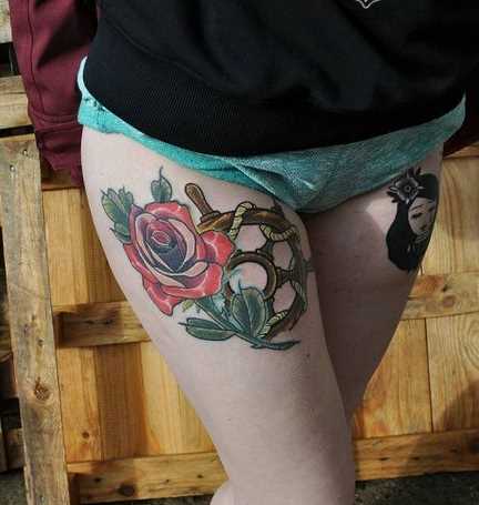 Tatuagem do volante com uma rosa na coxa da menina
