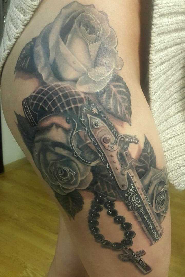 Tatuagem na coxa da menina - uma pistola e rosas