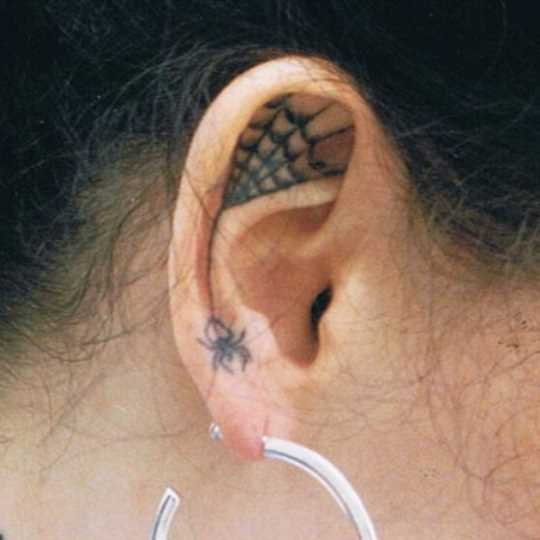 Tatuagem na orelha da menina - uma teia de aranha e a aranha