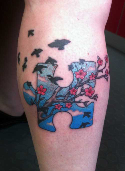 Tatuagem na perna de uma menina de quebra - cabeça e um ramo de cerejeira