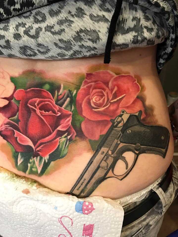 Tatuagem nas costas da menina - uma pistola e rosas