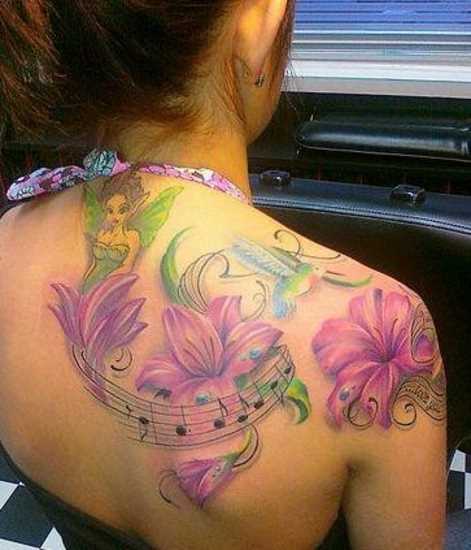 Tatuagem nas costas de uma menina lírios, beija-flores, fadas e as notas