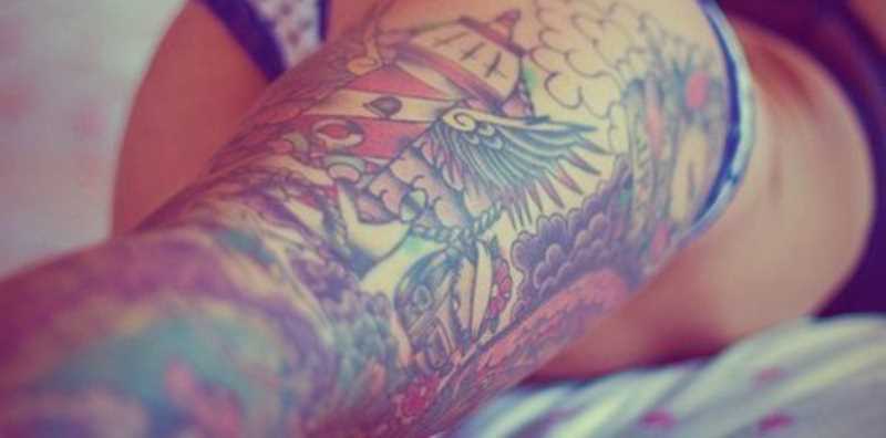 Tatuagem nas coxas da menina - farol, asas e âncora