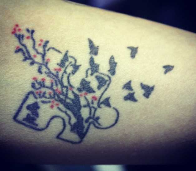 Tatuagem no antebraço de uma menina de quebra - cabeça com o ramo de cerejeira e os passarinhos