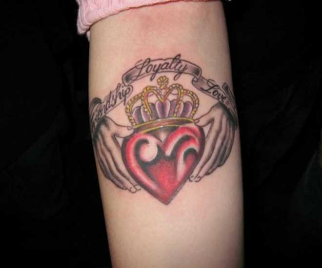 Tatuagem no antebraço de uma menina - o coração nas mãos, a inscrição e a coroa
