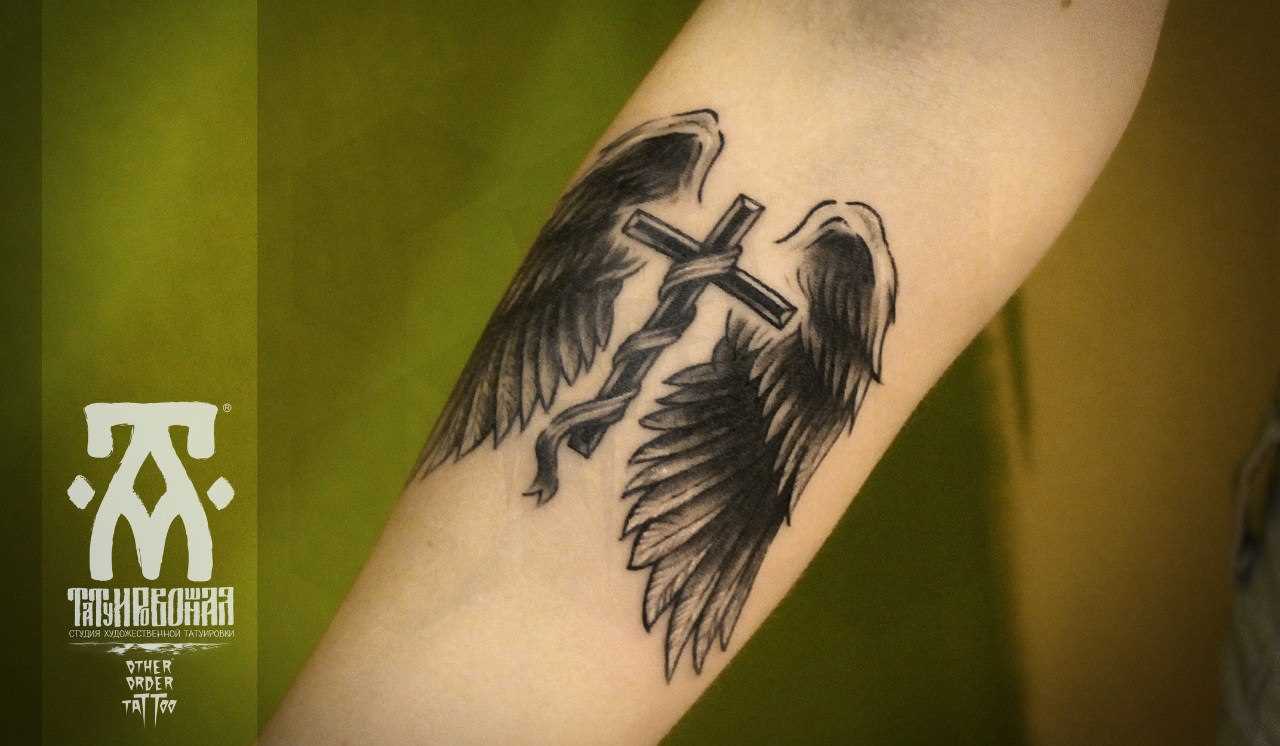 Tatuagem no antebraço do cara - a cruz e asas
