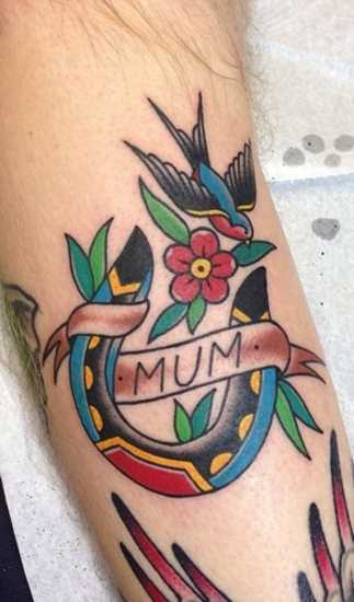 Tatuagem no braço de um cara - de- ferradura e a andorinha com flor