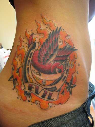 Tatuagem no lado da menina - ferradura, a inscrição, a andorinha, e o fogo