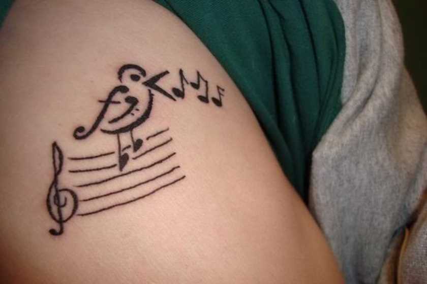 Tatuagem no ombro da menina - as notas da clave de sol e o pássaro
