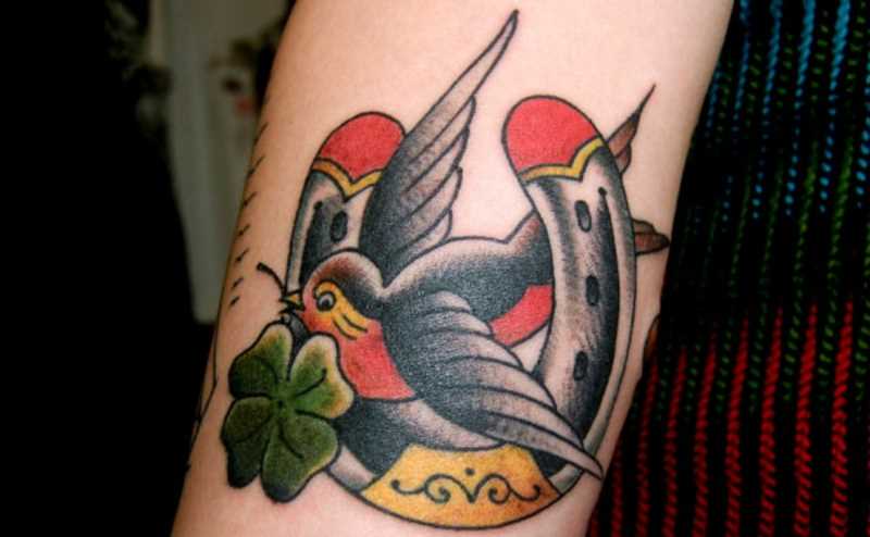 Tatuagem no ombro da menina - ferradura e a andorinha com um trevo