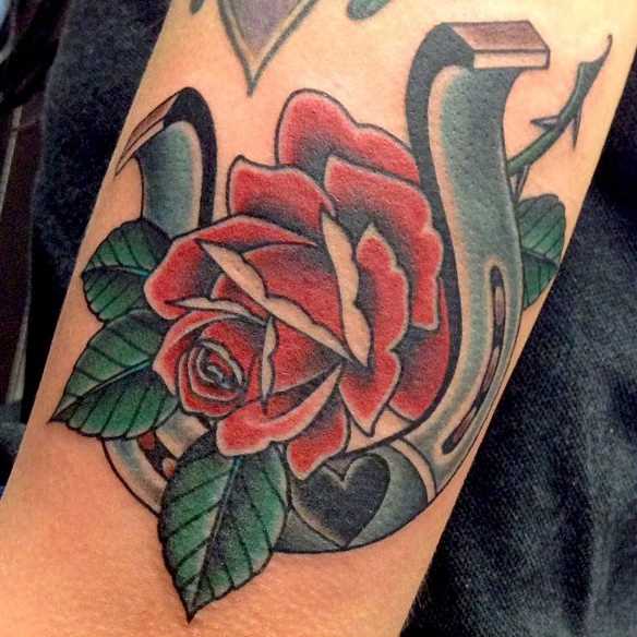 Tatuagem no ombro da menina - ferradura e uma rosa vermelha