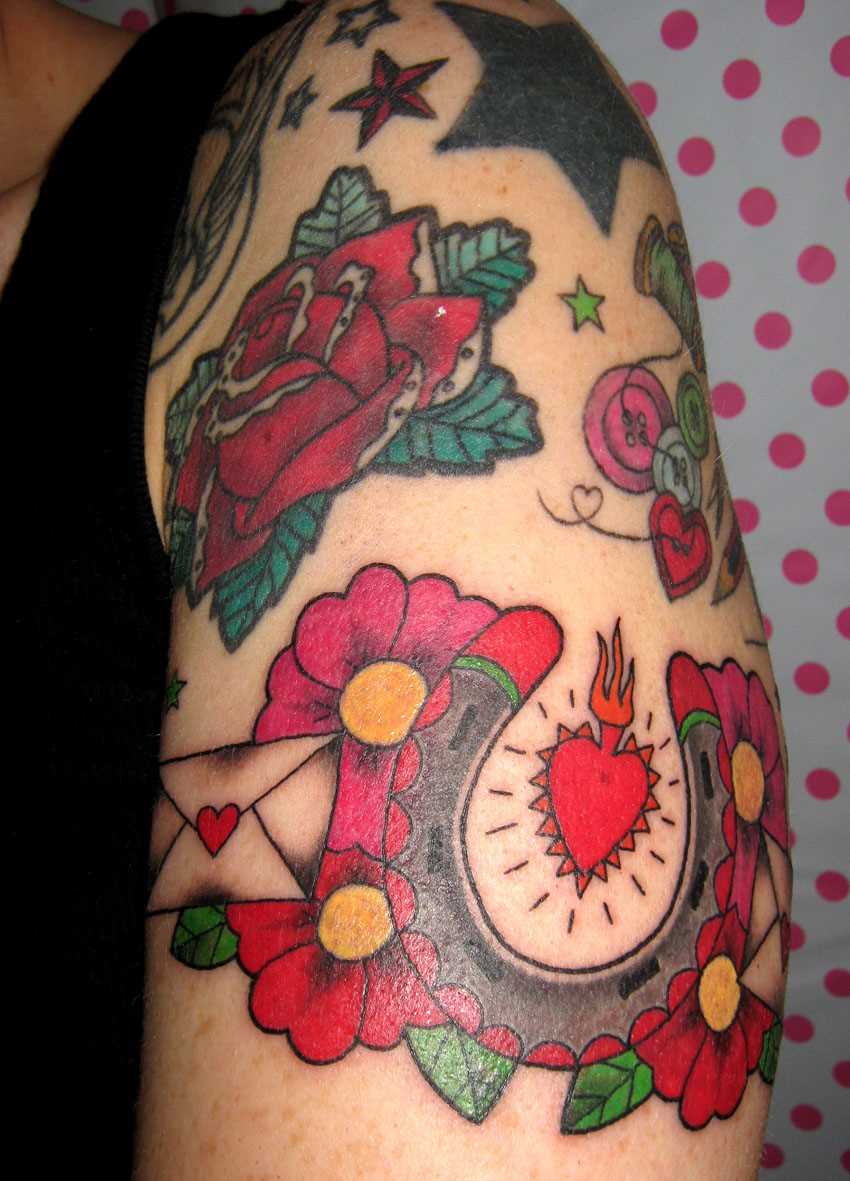 Tatuagem no ombro da menina - ferradura, flores e um envelope