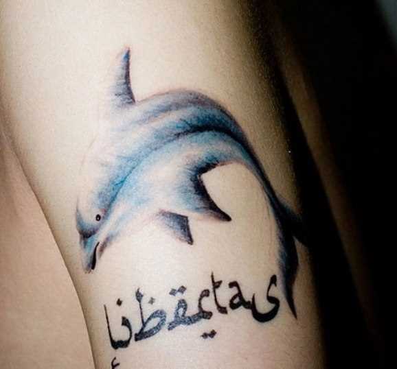 Tatuagem no ombro da menina - o golfinho e a inscrição