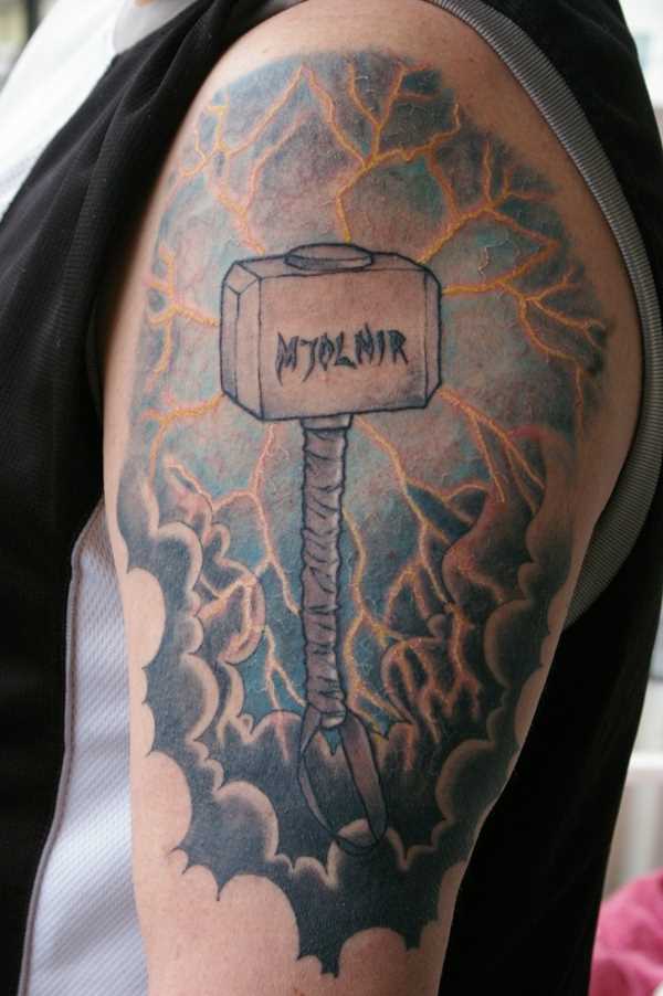 Tatuagem no ombro de um cara em forma de martelo e de um relâmpago no céu