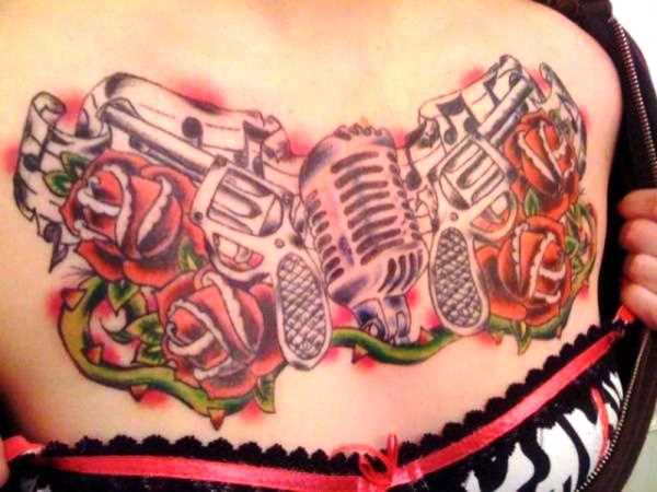 Tatuagem no peito da menina - pistolas, microfone e rosas