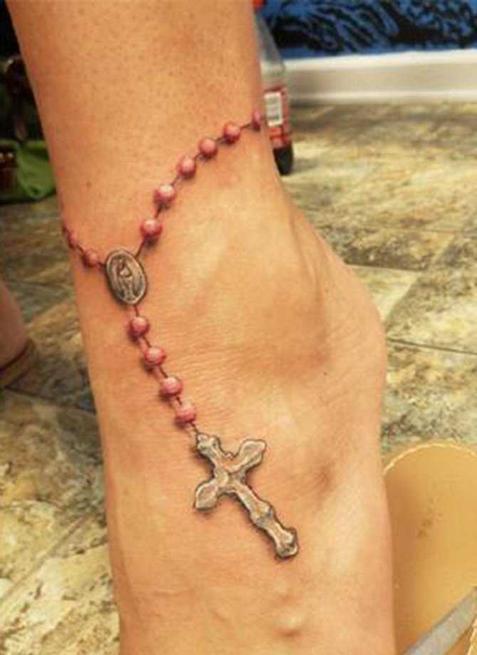 Tatuagem no tornozelo preto da menina - um colar com uma cruz