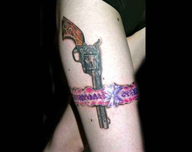 Tatuagem que a menina nos quadris em forma de revólver e cinta-liga