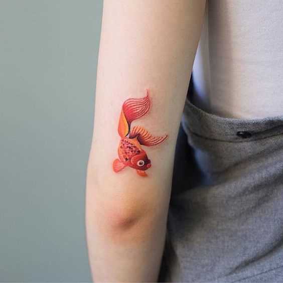 Uma pequena tatuagem de peixe de ouro na mão da menina
