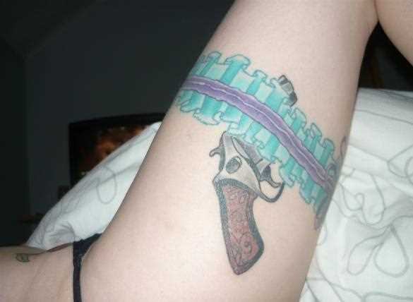 Uma tatuagem que a menina nos quadris em forma de revólver e cinta-liga